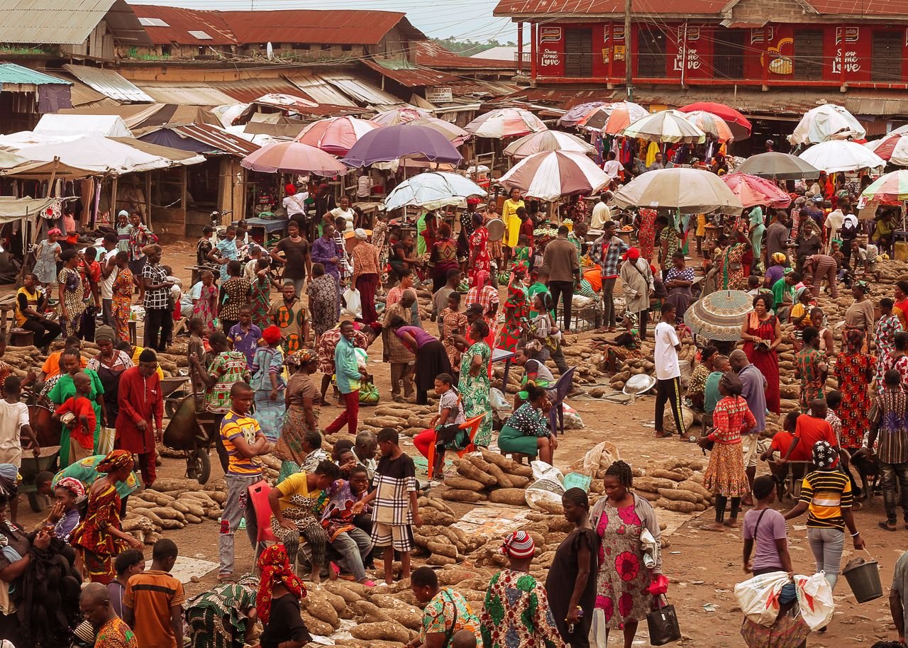 Lively outdoor African market with people selling goods under colorful umbrellas.